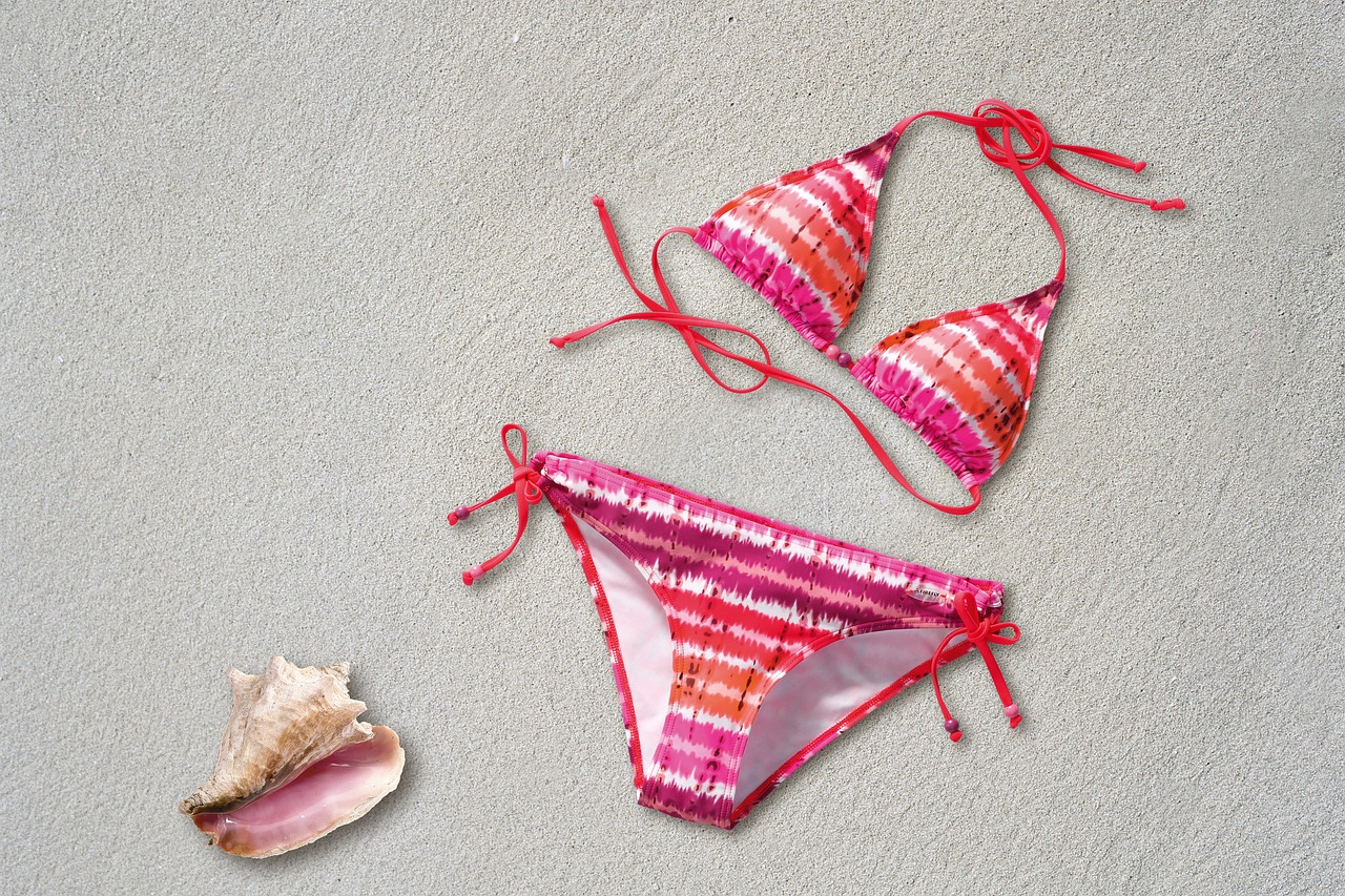 Pink and white striped bikini on the sand, next to seashell