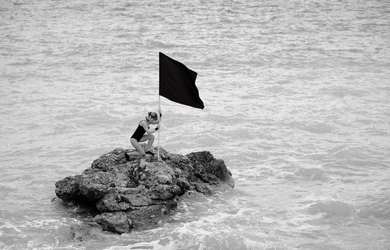 Woman planting a flag on a rock in the sea