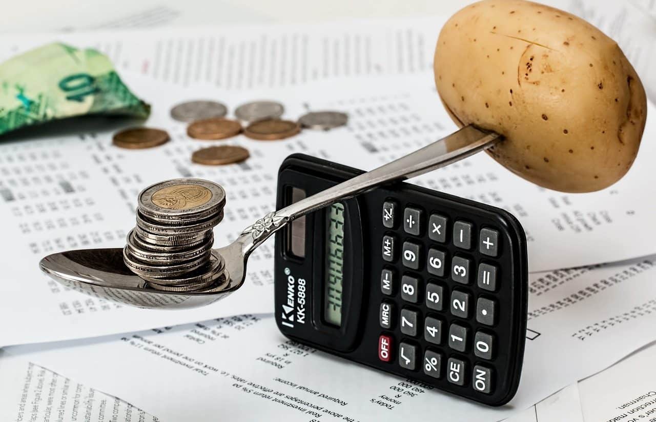 A potato and a stack of coins balanced on a spoon, on top of a calculator.