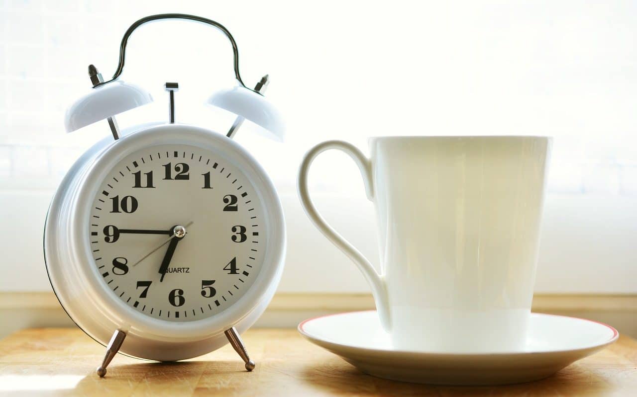 Alarm clock next to white cup