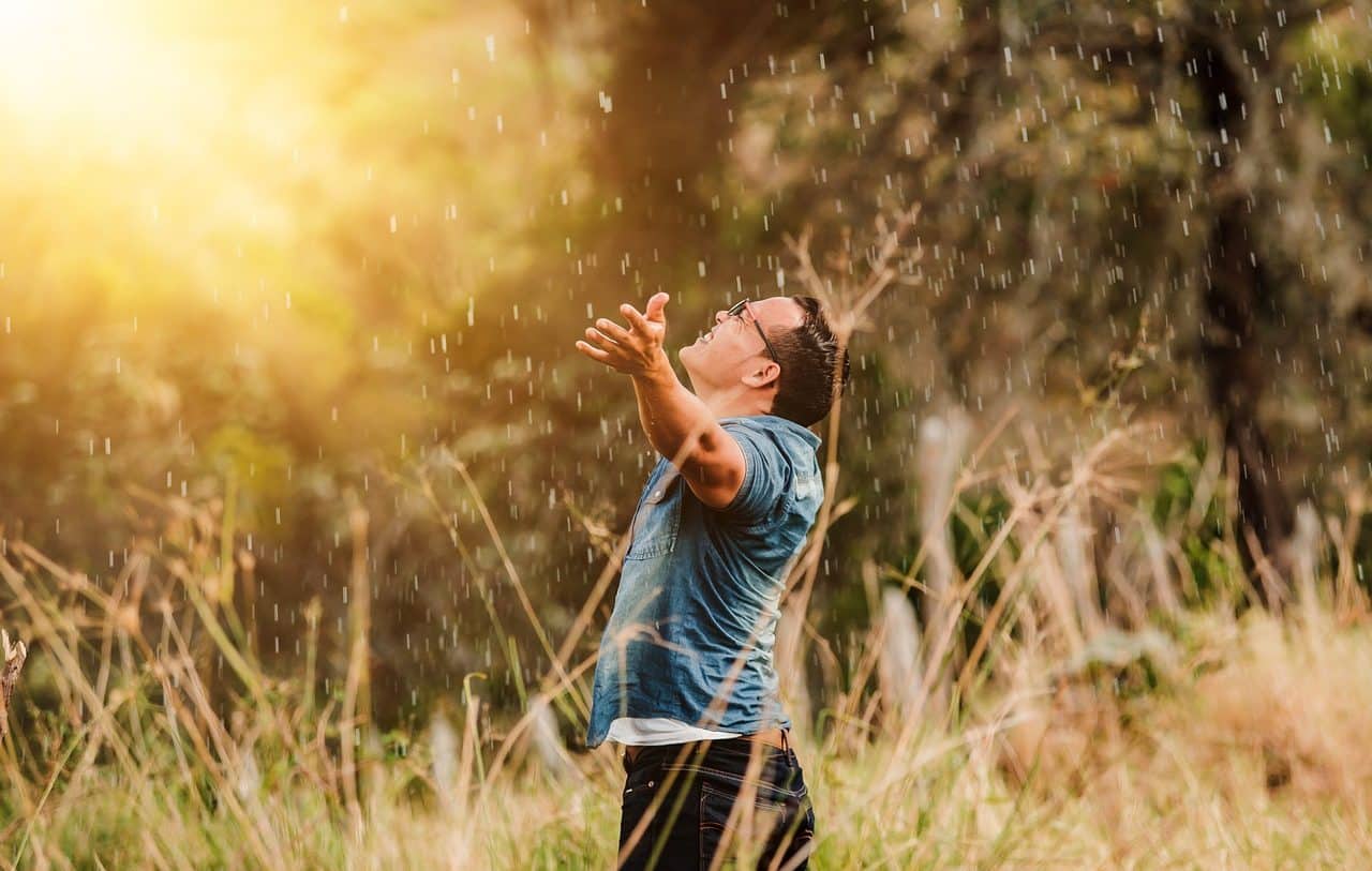 Young man receiving sunlight with open arms