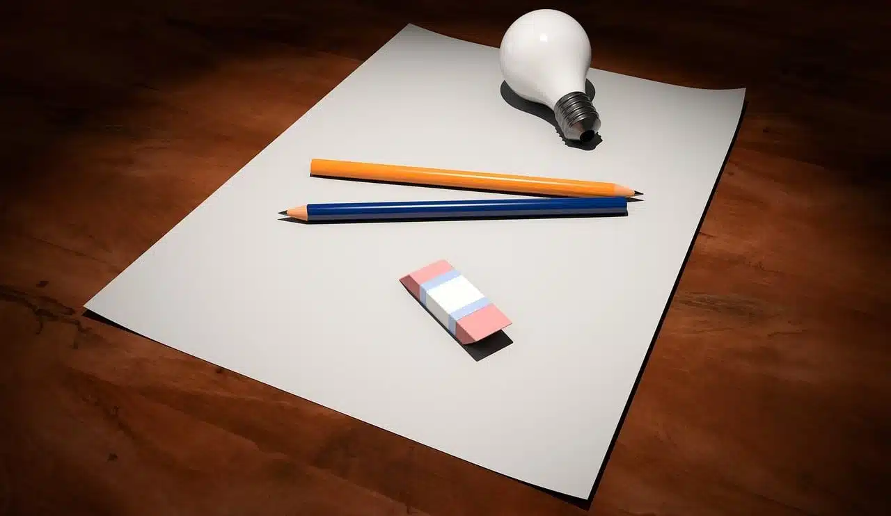 A light bulb, two pencils and an eraser on a blank sheet of paper