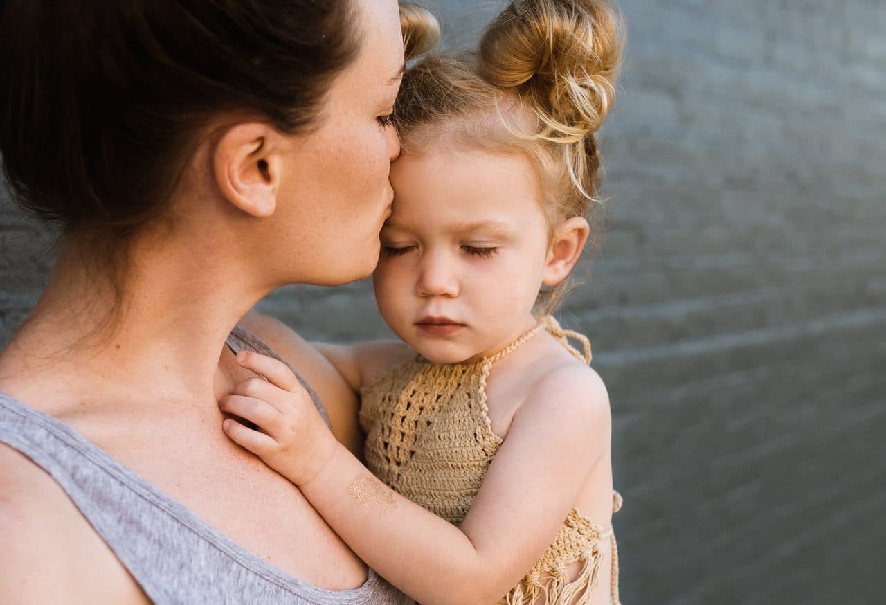 Mother holding her daughter in her arms and kissing her forehead