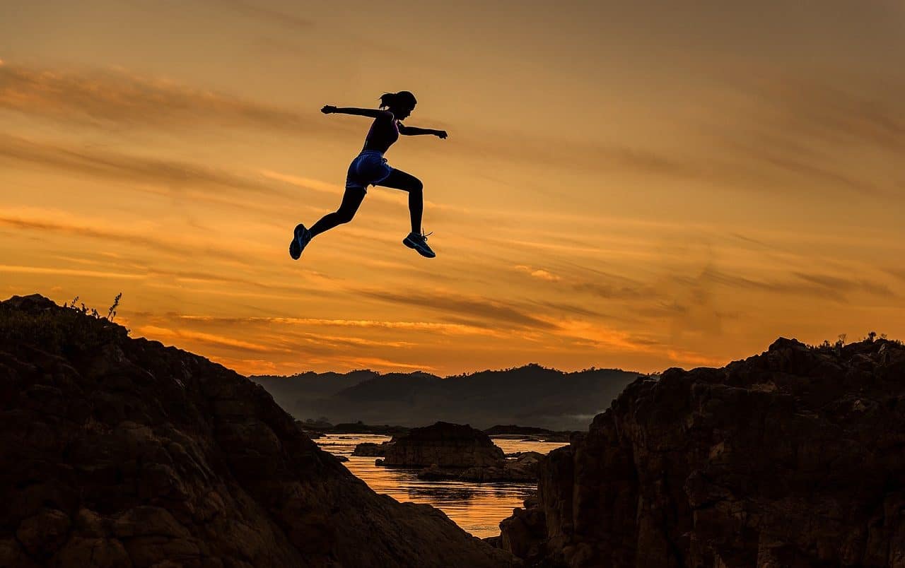 Woman jumping between two mountains at dawn