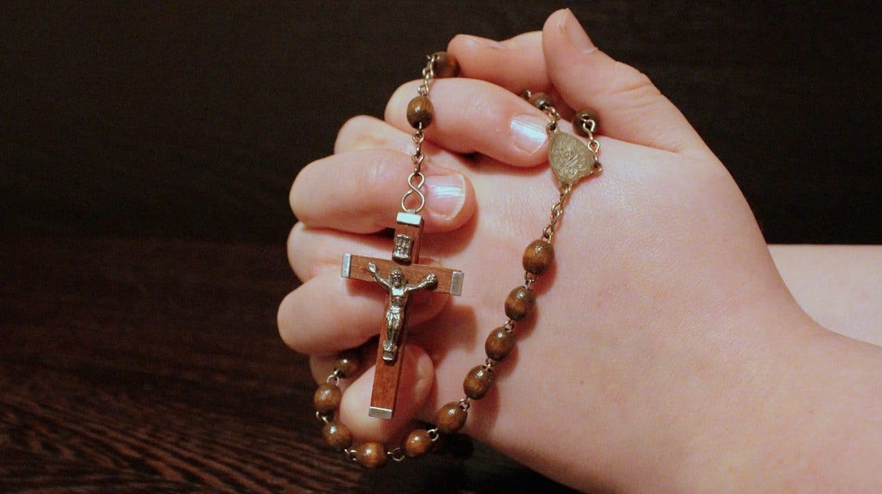 Woman holding a rosary with her hands joined in prayer position