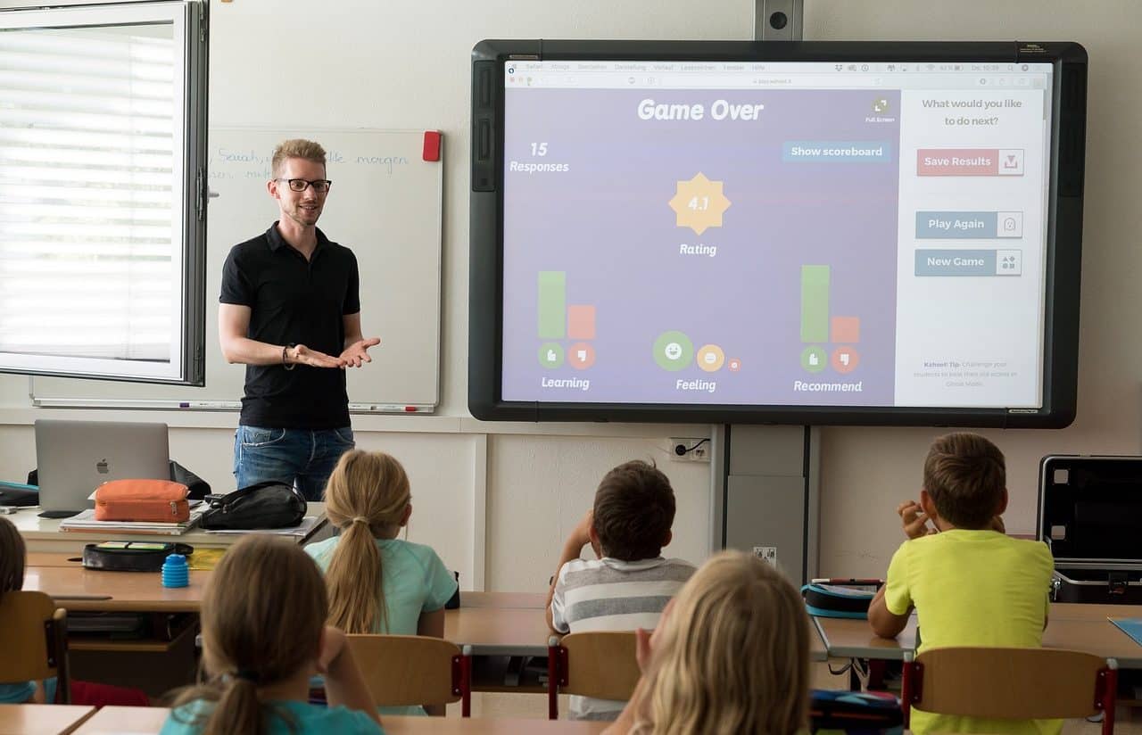 Teacher and children in the classroom watching a presentation on a large monitor