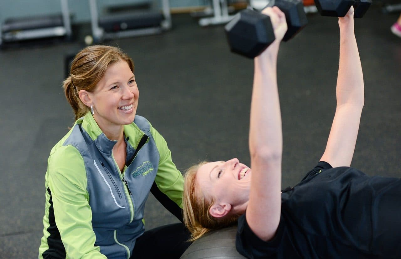 Young woman lifting weights in the gym with her personal trainer