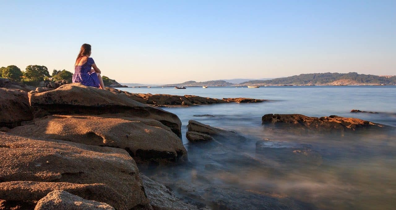 Woman sitting on rock next to water