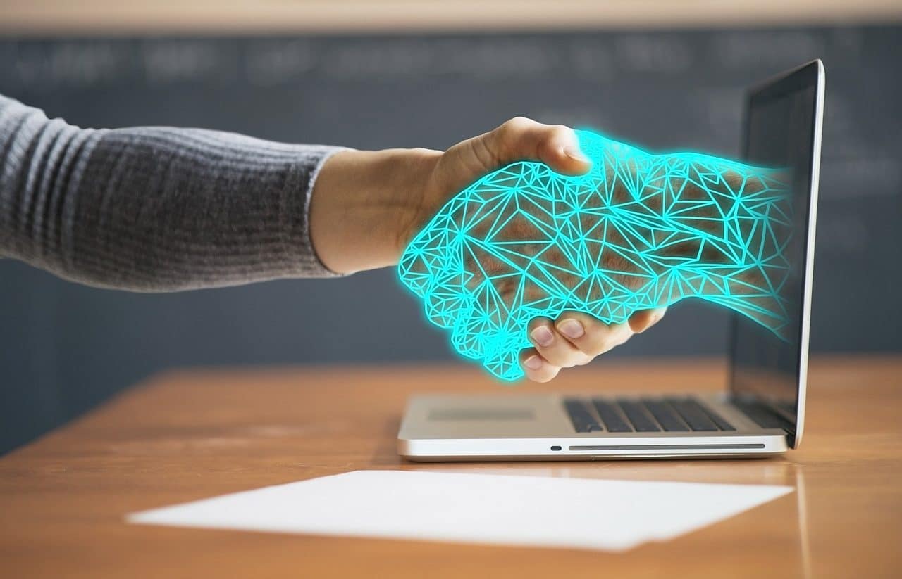 Man shaking his hand with a virtual one coming out of a laptop screen.