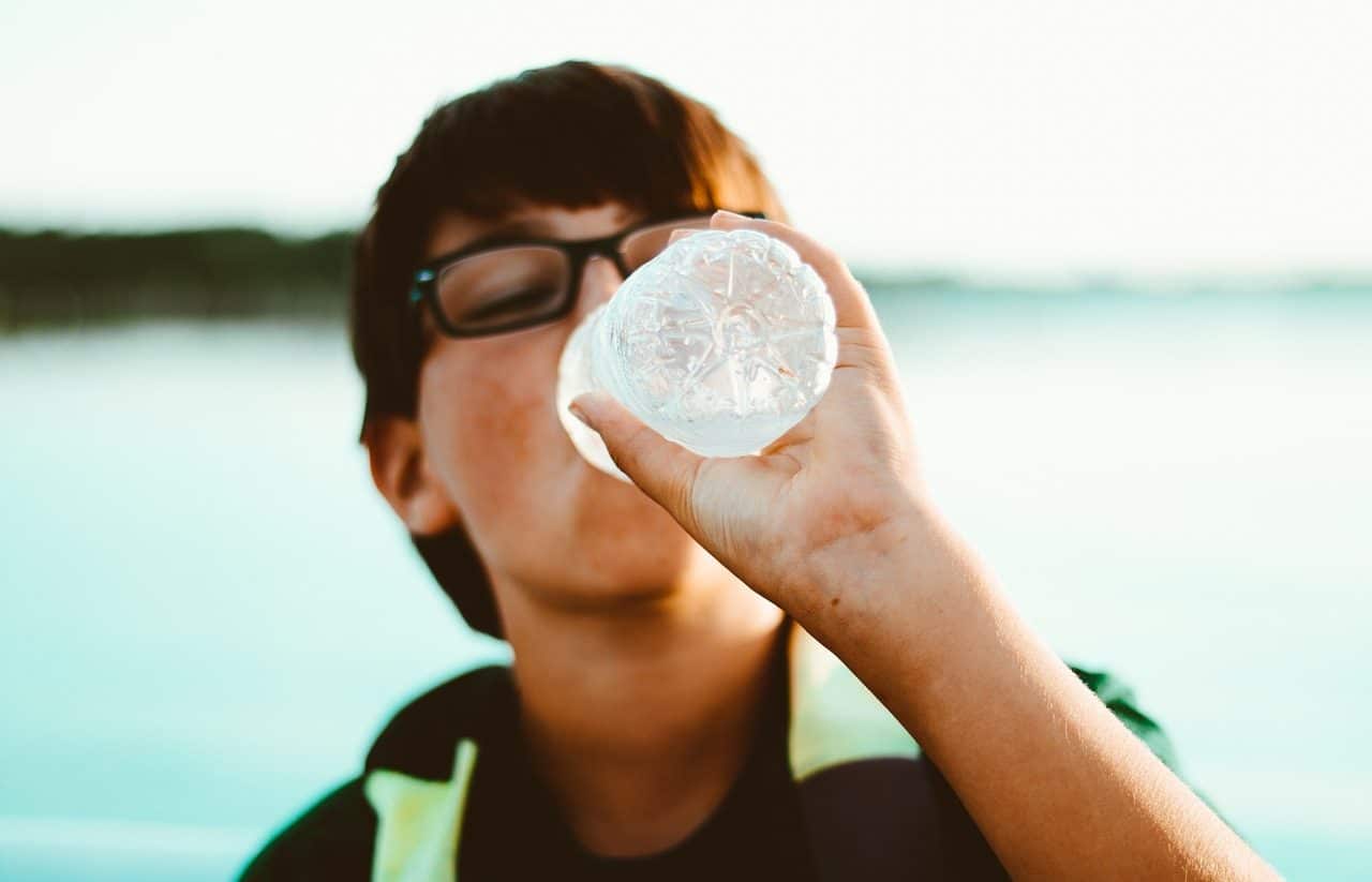 Woman drinking water from a bottle in front of the sea.