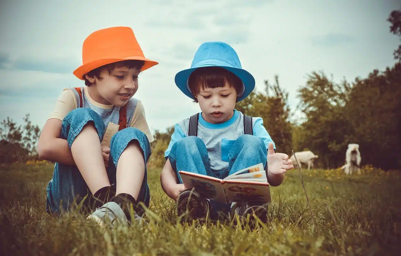 Two children reading a book sitting on the grass