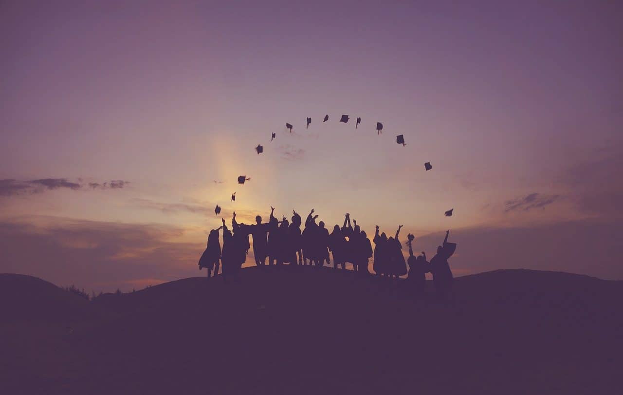 Several students throwing their caps into the air at sunset