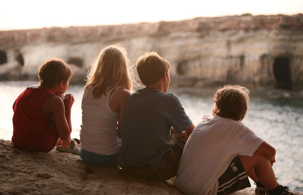 Four children sitting in front of a lake