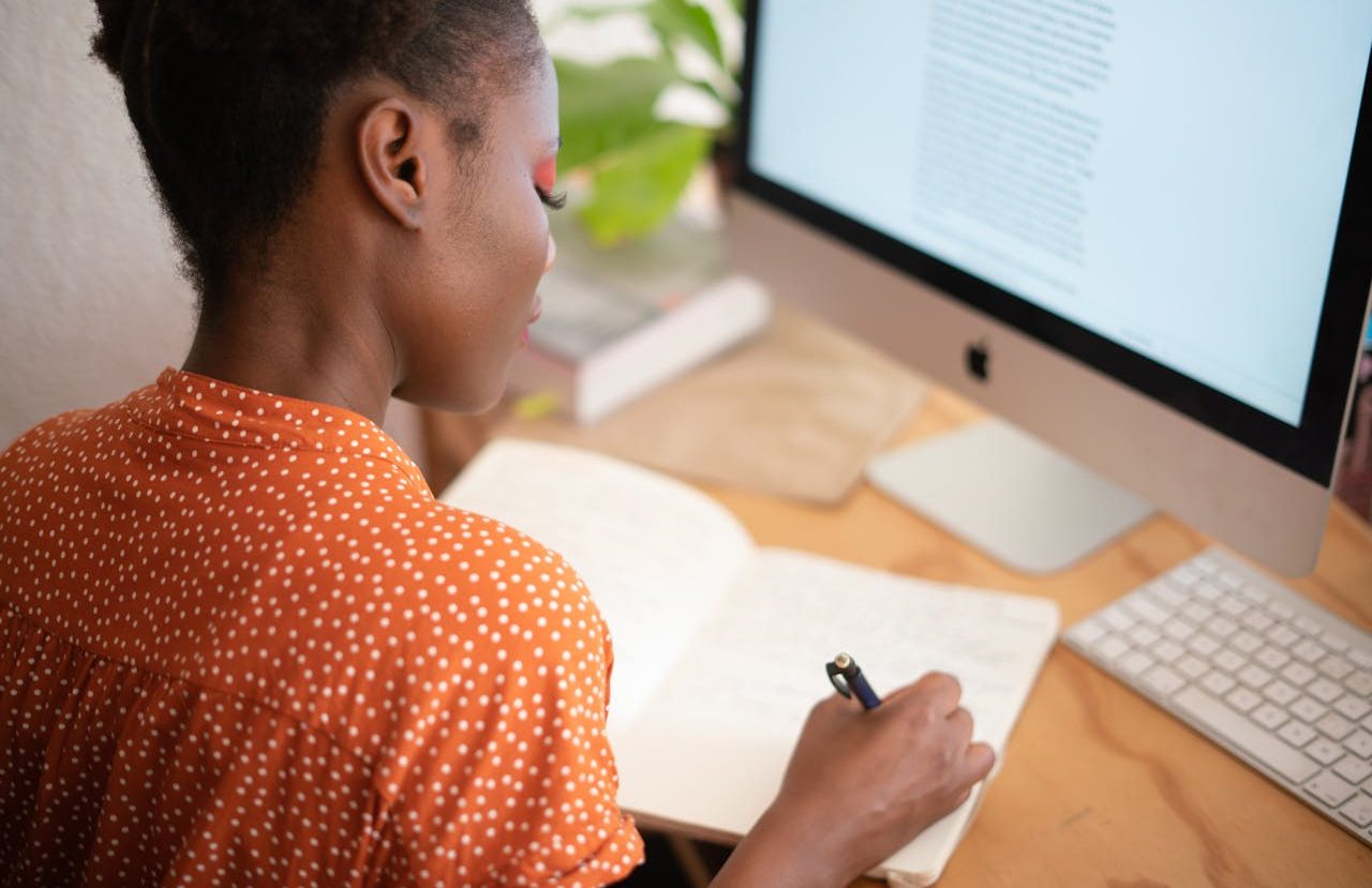 Woman writing in her notebook in front of her iMac.