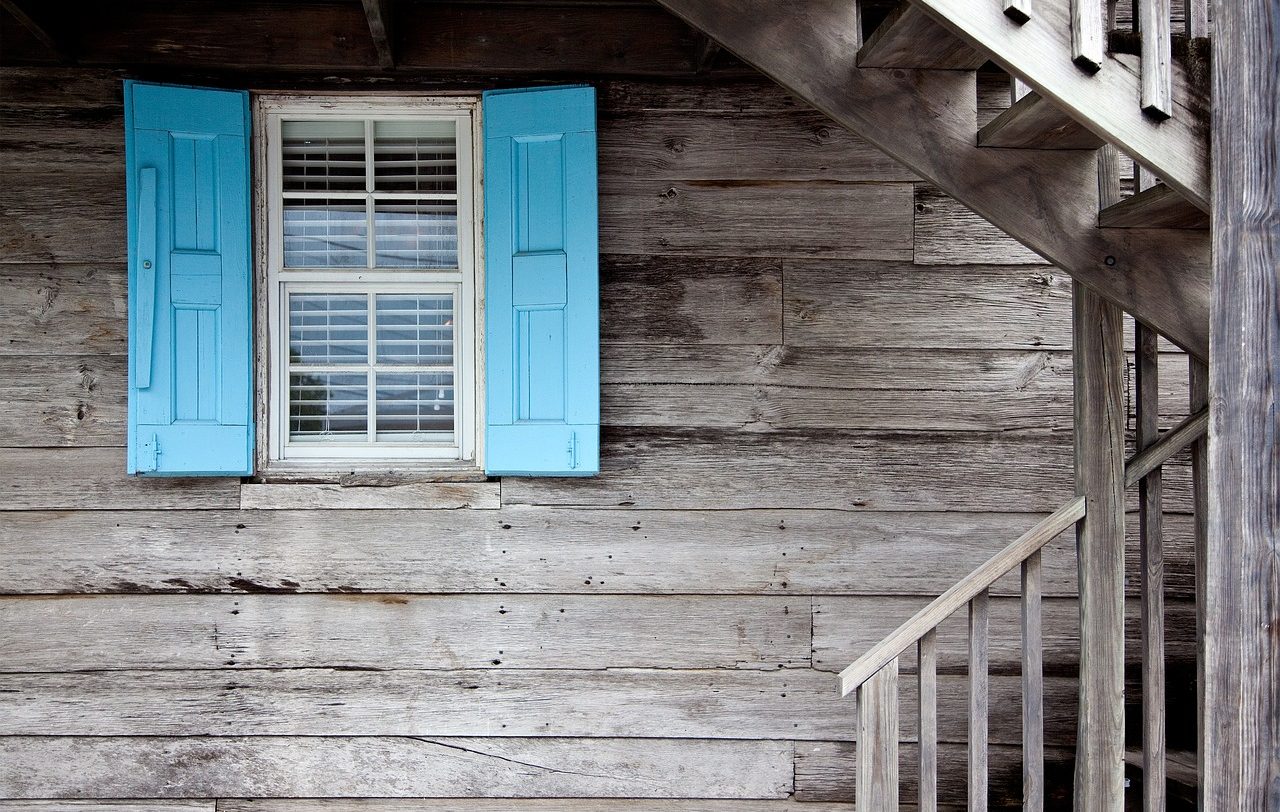 Gray wooden house. The window shutters are light blue.