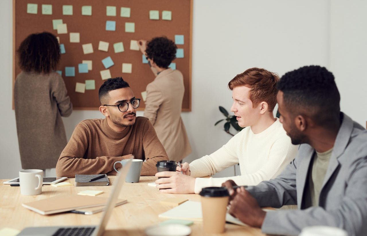 Work meeting: three men sitting and two women standing in the background