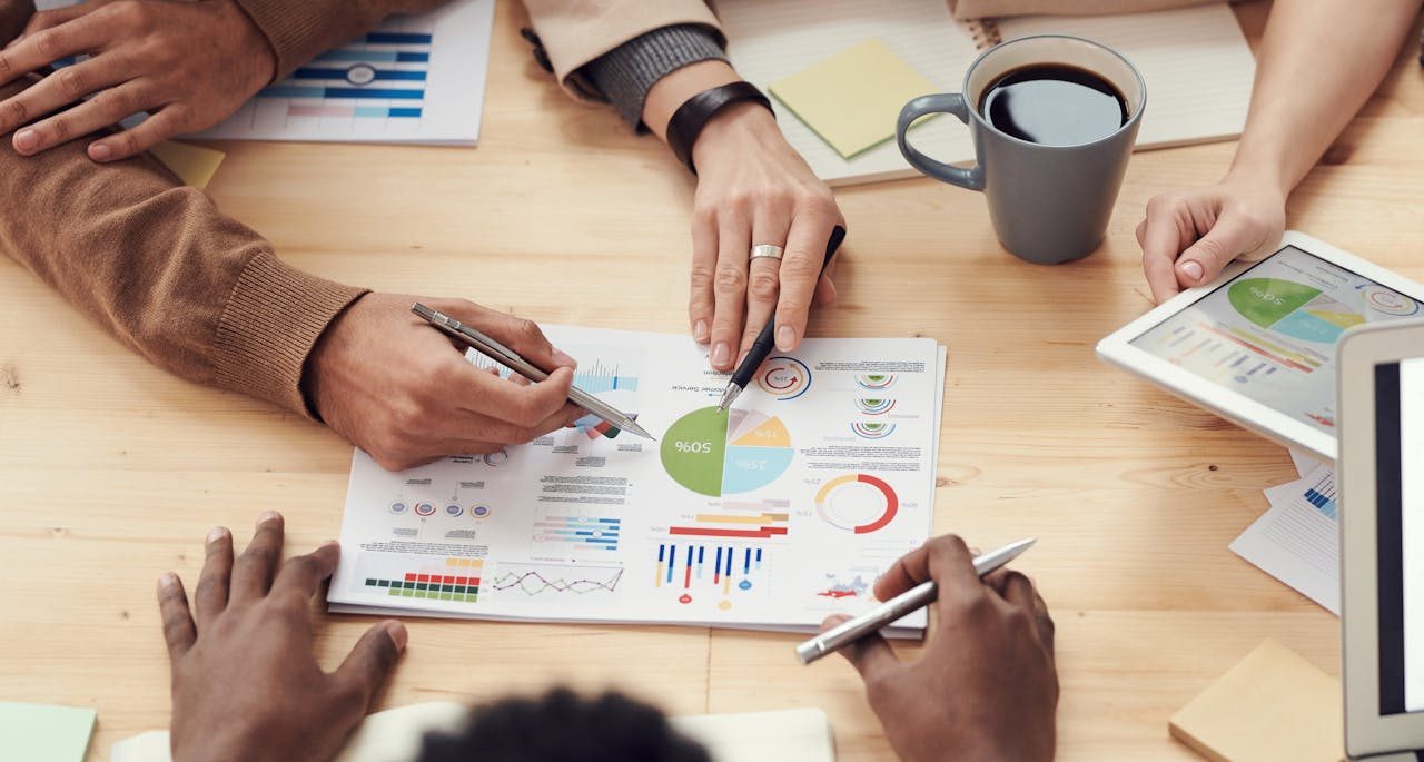 Several employees gathered analyzing various printed graphs on the table.