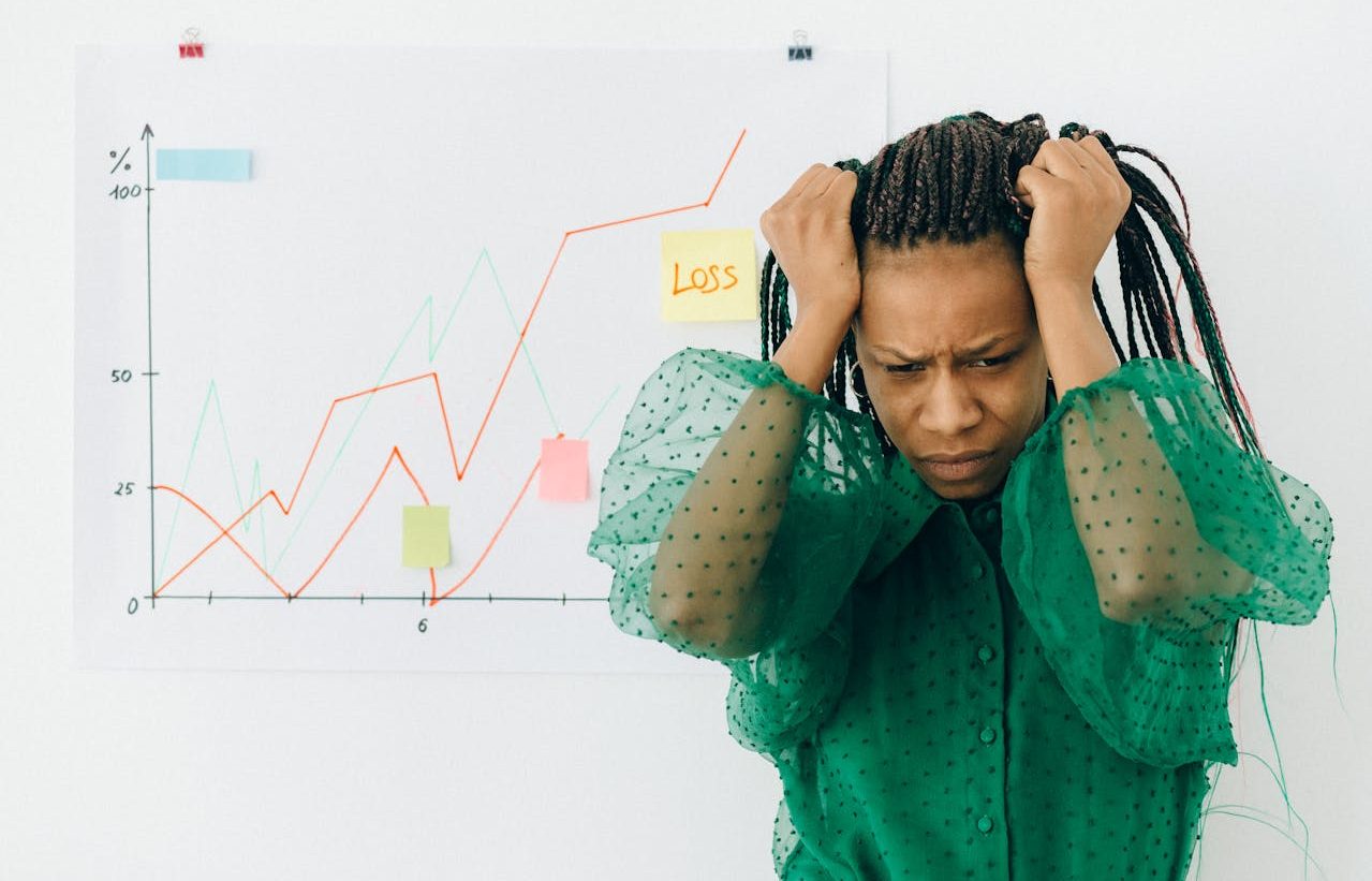 Woman clutching her head in front of a graph of financial losses.