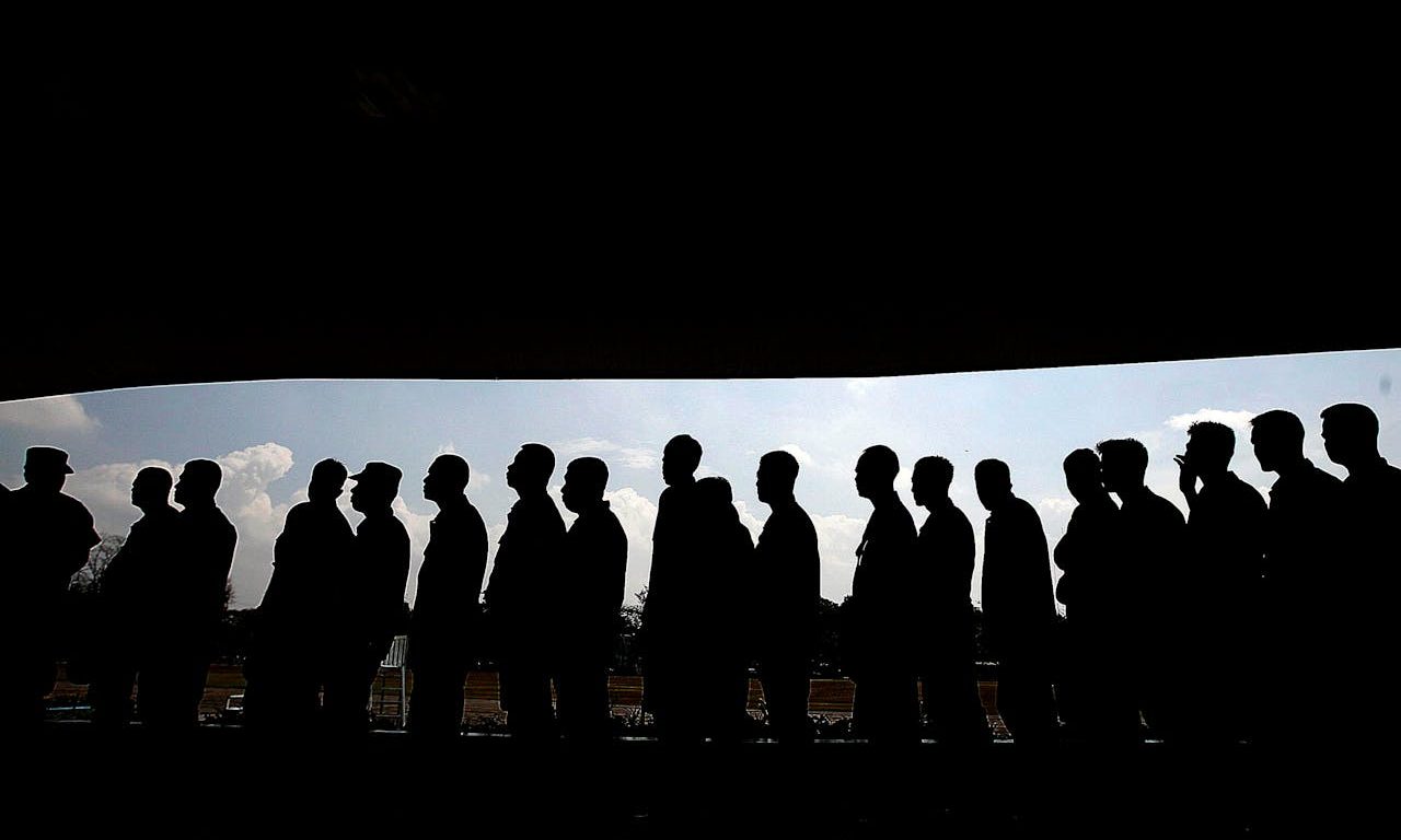 A line of people in the city. Their silhouettes can be seen, since they are illuminated from the background.